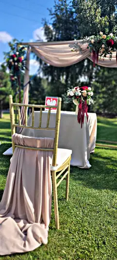 Zewnętrzna ceremonia ślubna z dekoracją w postaci kwiatów i tkanin, eleganckie krzesło na trawie. 