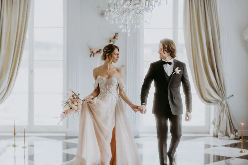  Para młoda na eleganckim ślubie w luksusowej sali, panna młoda w koronkowej sukni ślubnej, pan młody w eleganckim garniturze, delikatne kwiaty i dekoracje, romantyczna atmosfera. 