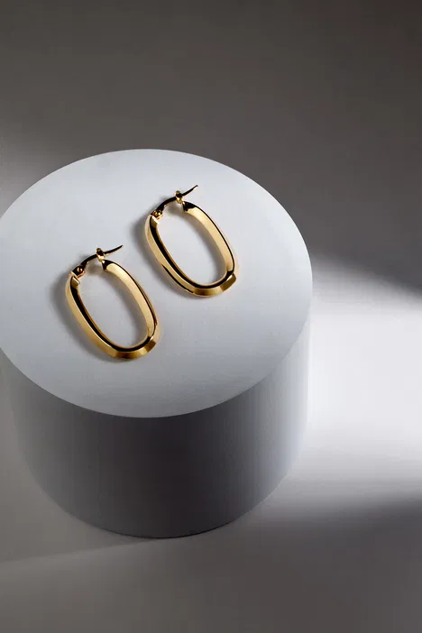 Złote kolczyki o owalnym kształcie na białym tle, elegancka biżuteria, minimalistyczny design.