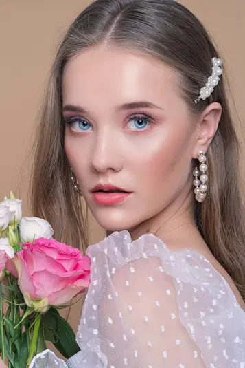  Portret młodej kobiety z niebieskimi oczami, ozdobionymi perłami włosami i kwiatami w dłoni, delikatny makijaż, elegancka sukienka w grochy, studio fotograficzne 