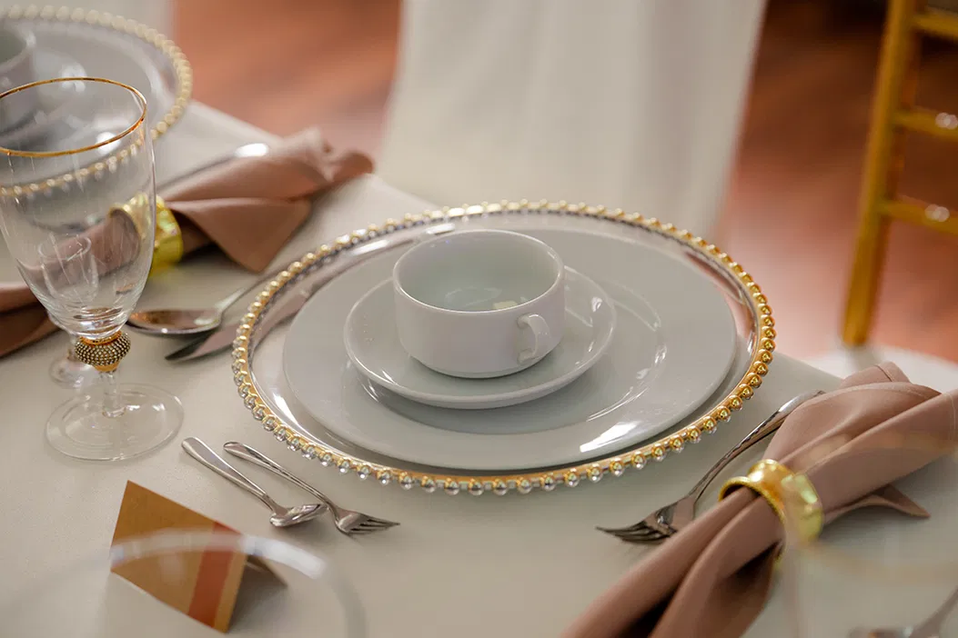 Elegancko nakryty stół z porcelanową zastawą, złotymi sztućcami i kieliszkiem, idealny na wesele lub bankiet.