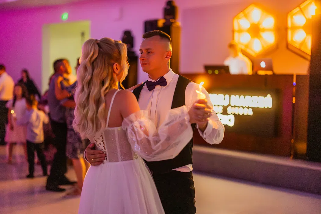 Para tańcząca na weselu, elegancko ubrana panna młoda i pan młody trzymający świeczki, w tle DJ i dekoracje świetlne.