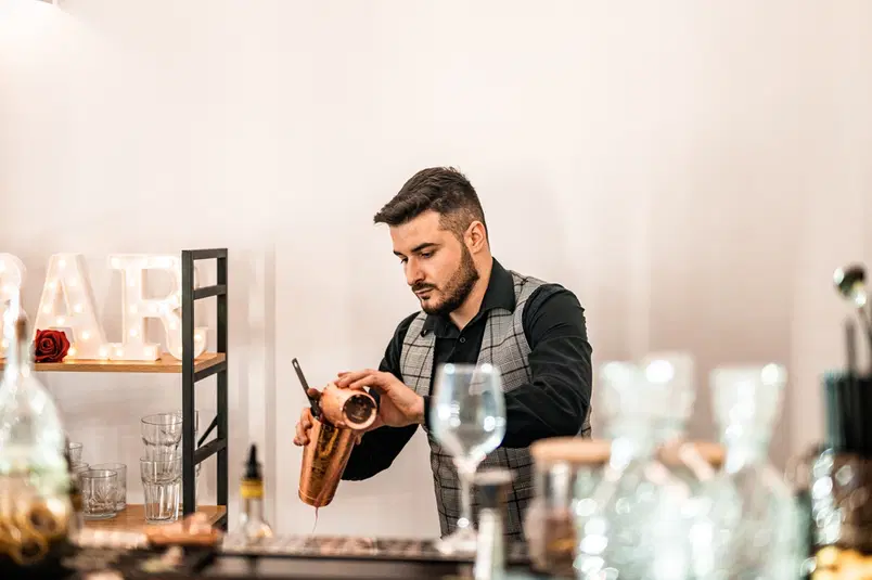 Barman przygotowujący koktajl w eleganckim barze, szklanki i akcesoria barmańskie na pierwszym planie. 