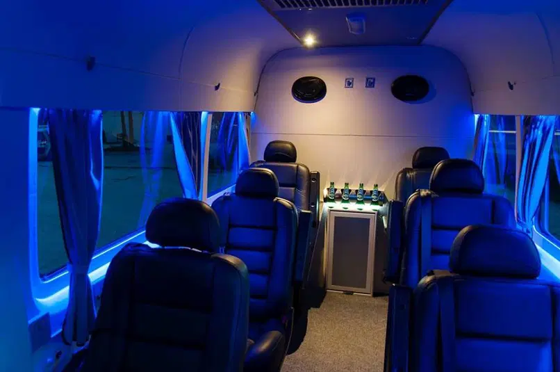  Luksusowe wnętrze vana z niebieskim oświetleniem LED, komfortowe skórzane siedzenia, mini bar z napojami, ekskluzywne wyposażenie do wynajmu autokarów. 
