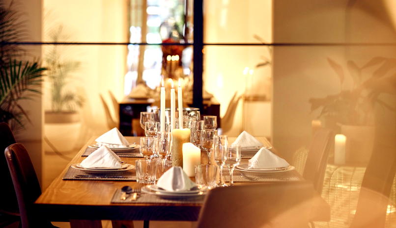  Elegancko nakryty stół jadalniany z białymi serwetkami, świecami i zastawą stołową w stylowym wnętrzu restauracji. 