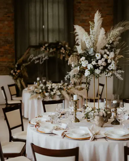  Elegancko udekorowana sala weselna z okrągłymi stołami, elegancką zastawą i kwiatowymi aranżacjami, styl rustykalny, przyjęcie weselne, romantyczna atmosfera. 