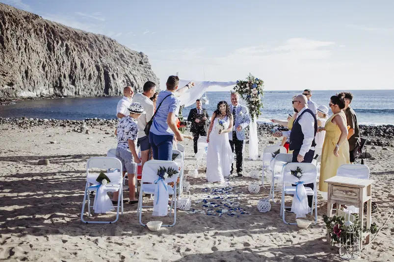  Ślub na plaży z widokiem na morze, para młoda otoczona gośćmi, dekoracje kwiatowe, słoneczny dzień, ceremonia plenerowa nad brzegiem oceanu. 