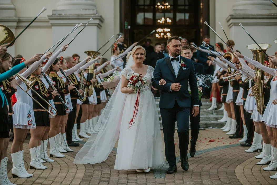Para młoda wychodząca z kościoła, otoczona przez orkiestrę dętą z uniesionymi instrumentami, ślub na świeżym powietrzu, uroczystość weselna w stylu tradycyjnym.