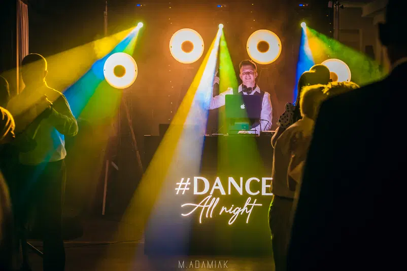  DJ prowadzi imprezę taneczną z kolorowym oświetleniem i hashtagiem #DanceAllNight na konsoli. 