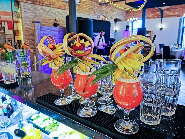 Kolorowe koktajle tropikalne z dekoracjami z owoców w eleganckich szklankach na barze, otoczone innymi drinkami i dekoracjami w klimatycznym wnętrzu restauracji. 