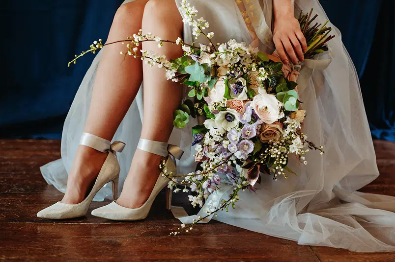  Ślubna sesja zdjęciowa, panna młoda w eleganckiej sukni z bukietem kwiatów, romantyczne buty na obcasie, piękne detale florystyczne. 