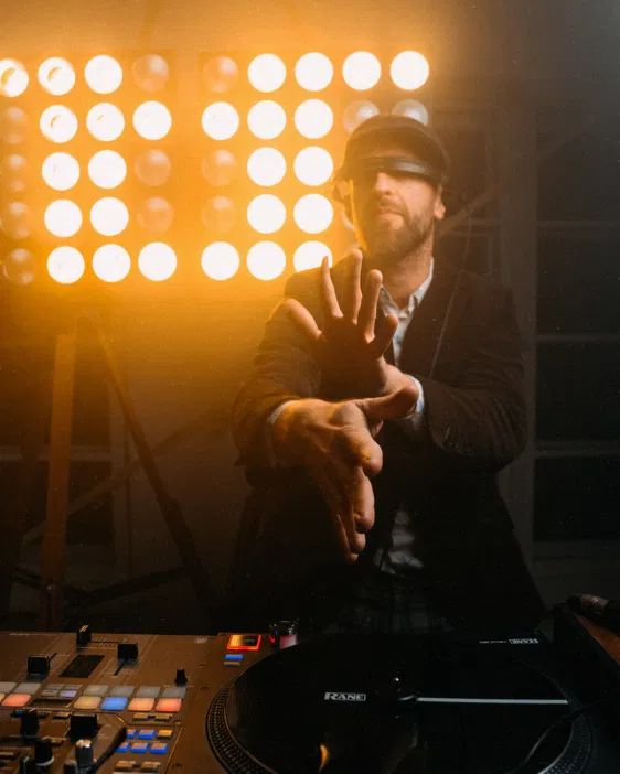 DJ przy gramofonie na imprezie z jasnym oświetleniem w tle.