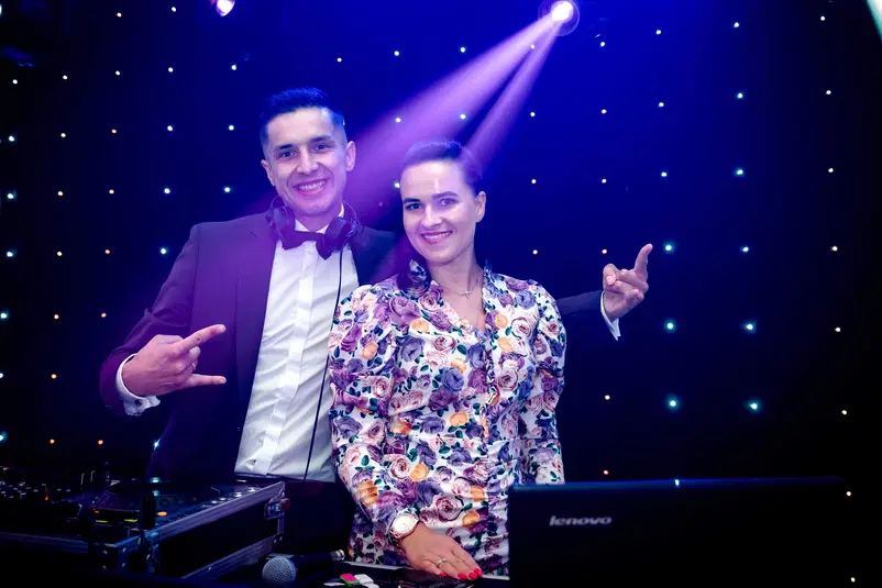  DJ i kobieta na imprezie z oświetleniem scenicznym, uśmiechają się i pozują przy sprzęcie DJ. 