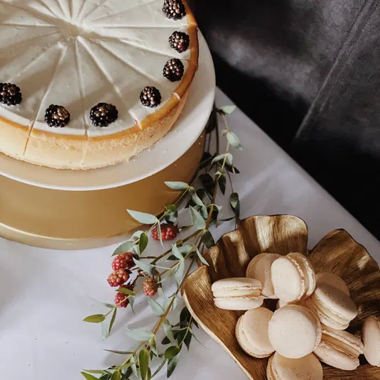  Tort serowy ozdobiony jeżynami i makaroniki na stole dekoracyjnym. 