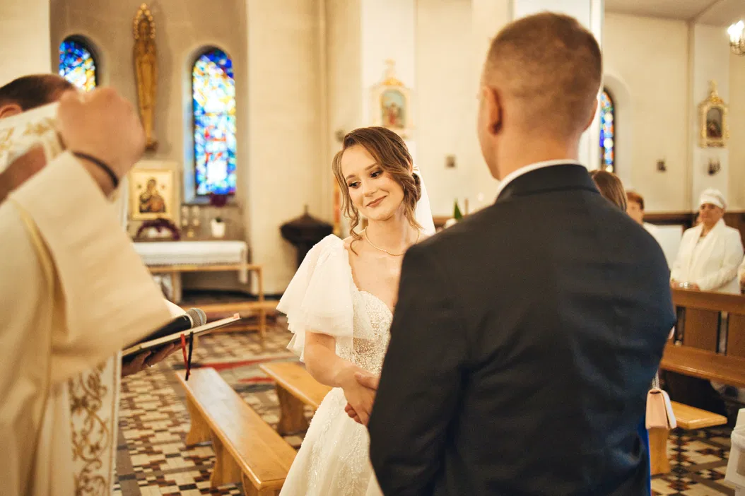 Ślub w kościele - Para młoda podczas ceremonii zaślubin, wymiana przysięgi małżeńskiej, piękna panna młoda i pan młody w eleganckim garniturze, w tle witraże i zgromadzeni goście.