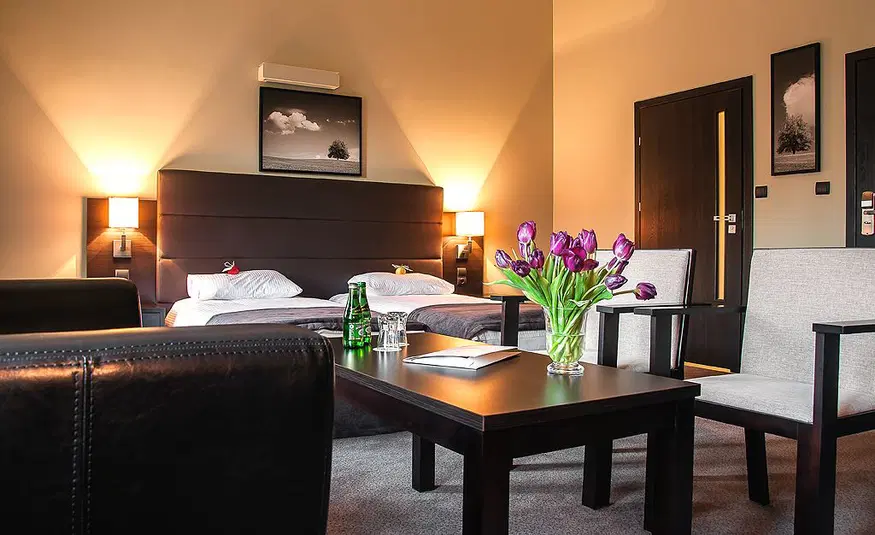  Luksusowy pokój hotelowy z podwójnym łóżkiem, eleganckimi fotelami i wazonem fioletowych tulipanów na stoliku kawowym. 