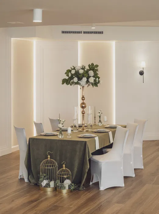 Elegancko udekorowany stół w jadalni z zielonym obrusem, białymi krzesłami i wysokim wazonem z kwiatami, nowoczesne wnętrze.