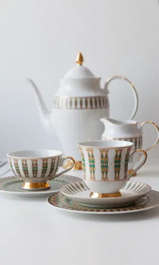  Luksusowy zestaw herbaciany z porcelany, w skład którego wchodzi czajnik, filiżanki i spodeczki, ozdobione złotymi i zielonymi detalami. 