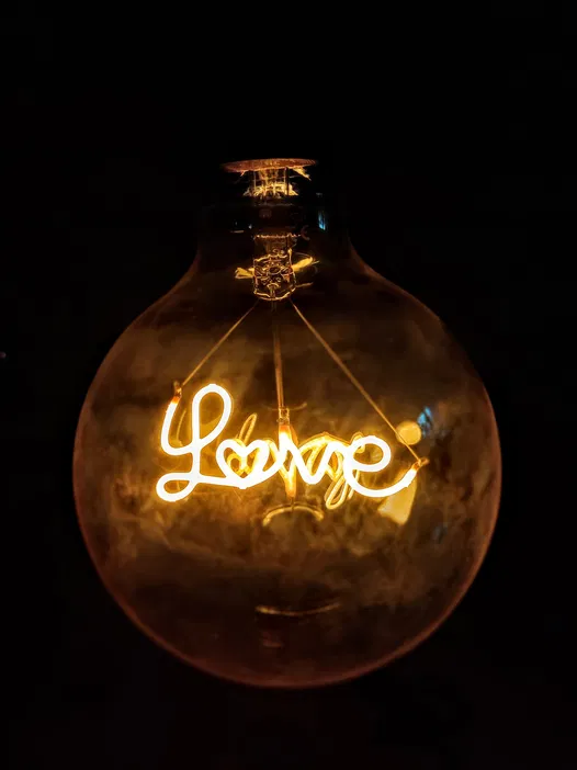 Żarówka z napisem Love świecąca na czarnym tle, symbol miłości i romantyzmu.