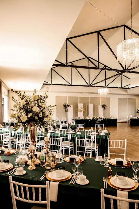 Elegancka sala bankietowa z białymi krzesłami, zielonymi obrusami i dekoracjami kwiatowymi, przygotowana na przyjęcie weselne.