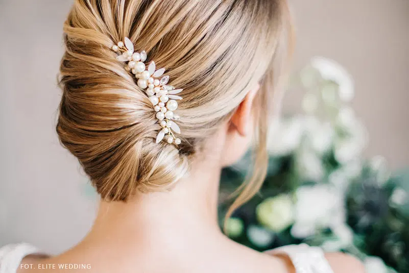  Elegancka fryzura ślubna z ozdobną spinką i perłami, upięta na blond włosach. 