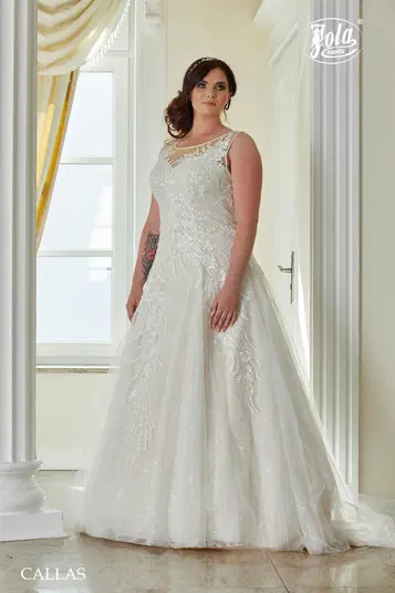  Kobieta w eleganckiej sukni ślubnej z koronkowymi zdobieniami stoi w jasnym wnętrzu. 