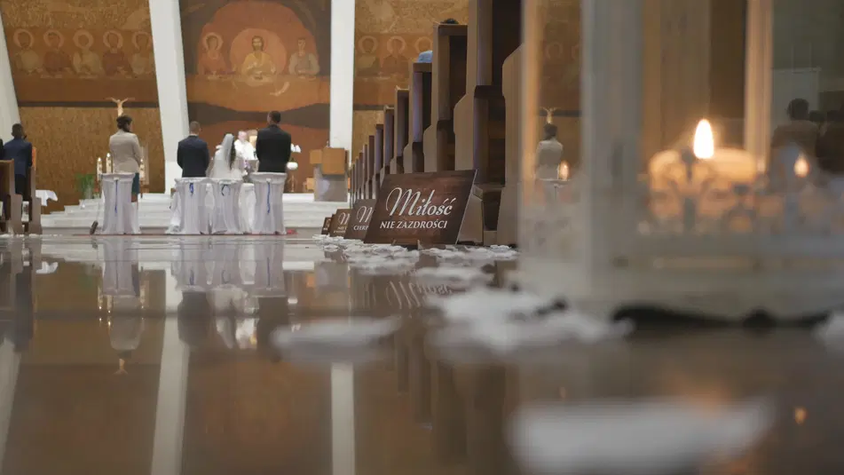  Ceremonia ślubna w kościele z parą młodą przed ołtarzem, dekoracje weselne, napis Miłość nie zazdrości, romantyczne oświetlenie świec, atmosfera sakralna. 