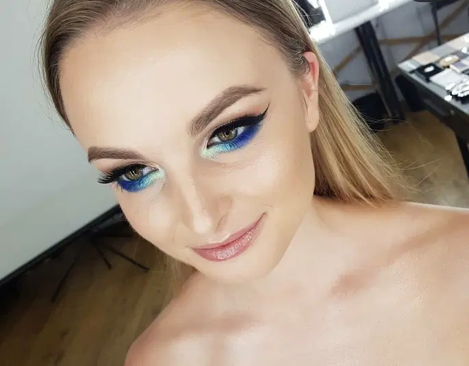  Blond kobieta z artystycznym makijażem oczu w niebiesko-zielonych odcieniach, fotografia portretowa w jasnym, dobrze oświetlonym pomieszczeniu. 