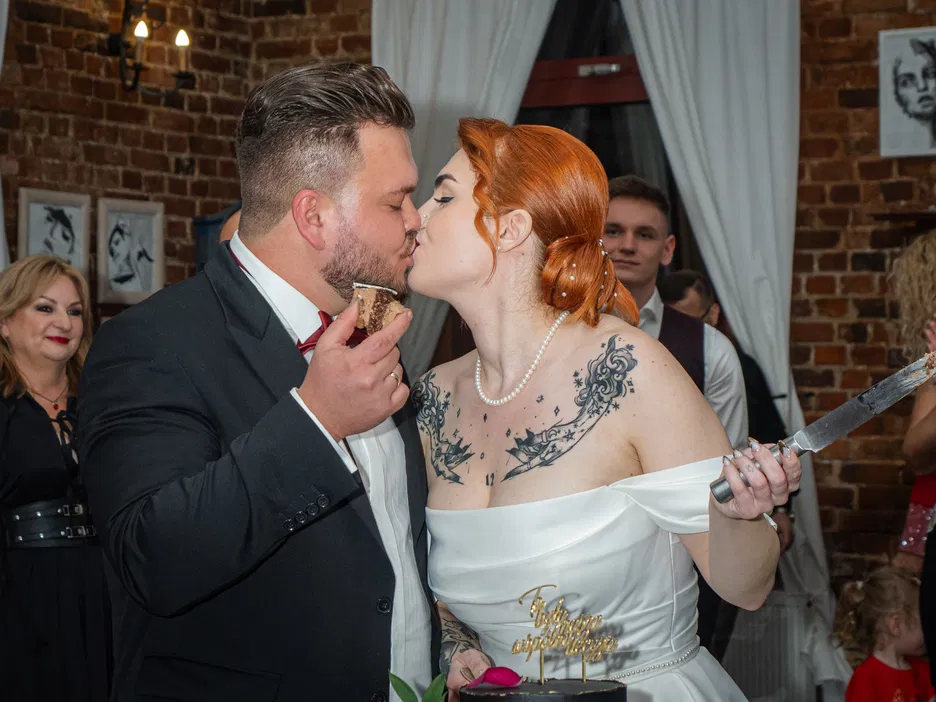 Para młoda podczas krojenia tortu weselnego i pocałunku, ceremonia ślubna, sala weselna z gośćmi.