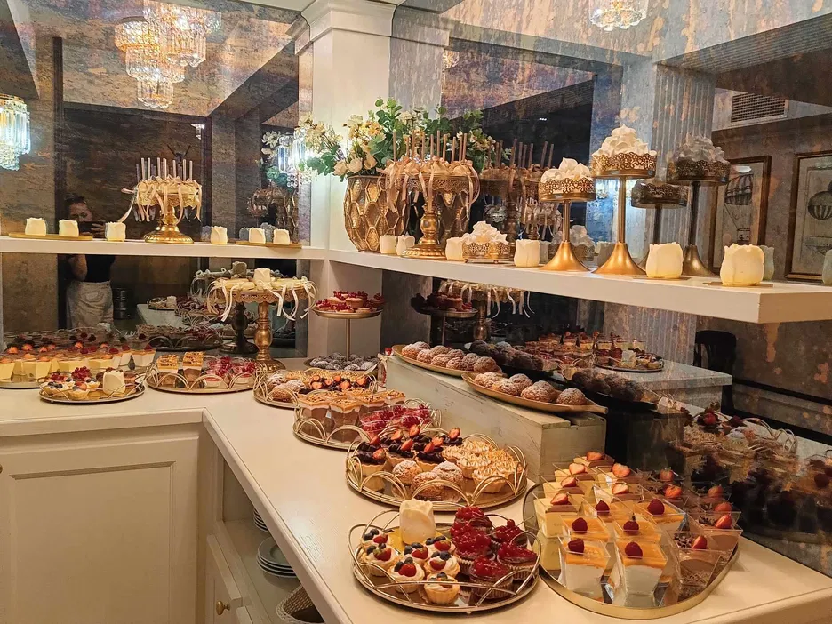 Luksusowy bufet deserowy z eleganckimi ciastkami i ciastami na złotych stojakach, w eleganckiej restauracji, złote dekoracje, romantyczna atmosfera.