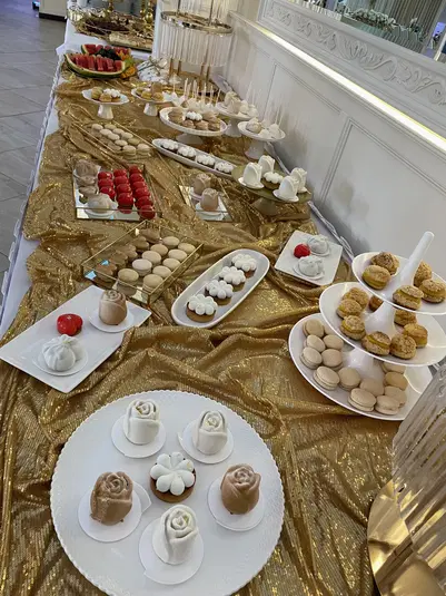  Stół weselny z eleganckimi deserami na złotym obrusie: makaroniki, ciastka w kształcie róż, owoce oraz dekoracje. 