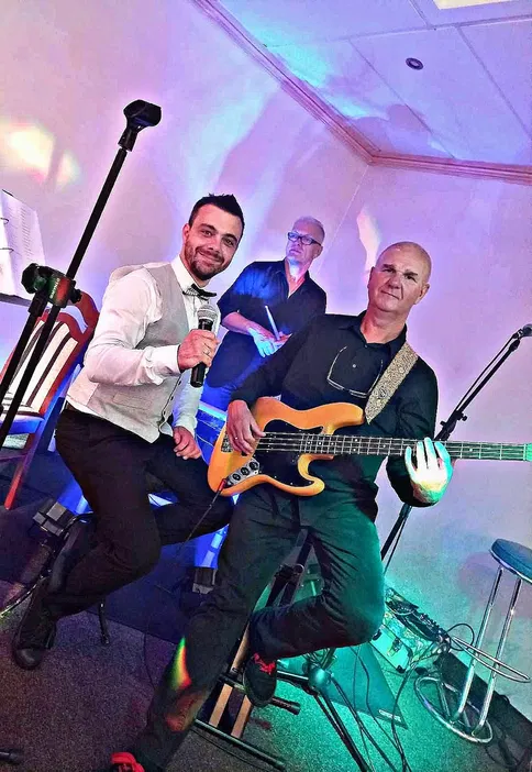 Muzycy grający na imprezie, piosenkarz z mikrofonem i gitarzysta z gitarą basową, jasne oświetlenie sceniczne.