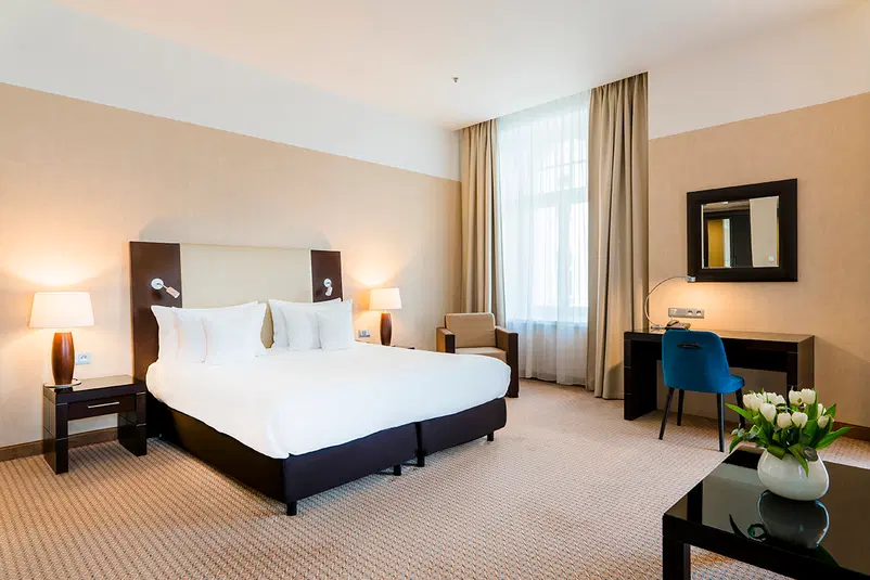  Elegancko urządzony pokój hotelowy z dużym łóżkiem, stylowymi lampkami nocnymi i biurkiem przy oknie. 