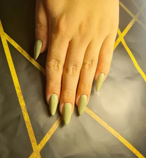  Elegancki manicure w oliwkowym kolorze na dłoni z długimi, migdałowymi paznokciami, na tle geometrycznego wzoru. 
