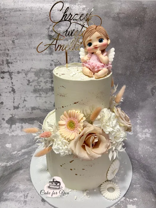 Two-tiered christening cake with floral decorations and an angel figurine topper.