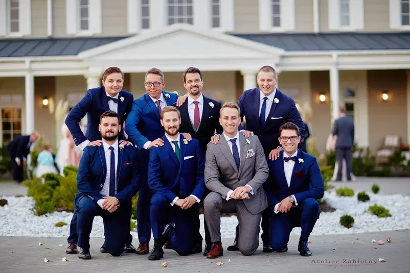  Grupa mężczyzn w eleganckich garniturach pozuje na zewnątrz przed budynkiem, ślub, elegancki strój, stylowa fotografia. 