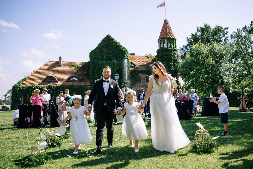 Ślubna para młoda z dziećmi w ogrodzie, ceremonia na świeżym powietrzu przed zamkiem, letnia pogoda.
