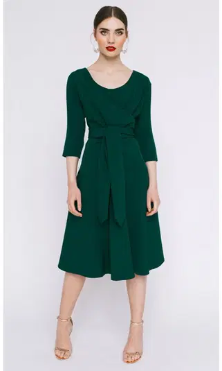  Modelka w eleganckiej zielonej sukience z wiązaniem, stojąc na białym tle. 