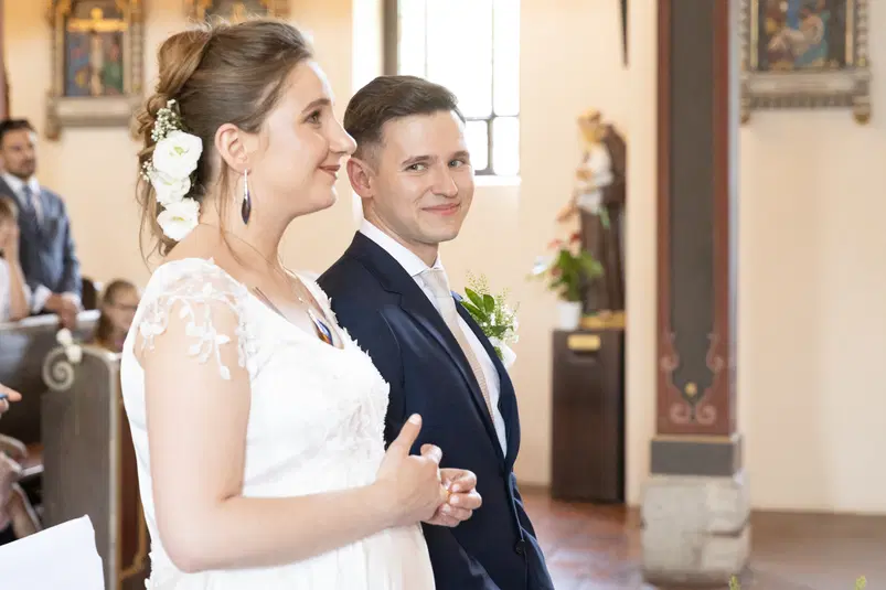  Para młoda w kościele podczas ceremonii ślubnej, panna młoda w białej sukni z kwiatami we włosach, pan młody w eleganckim garniturze. 