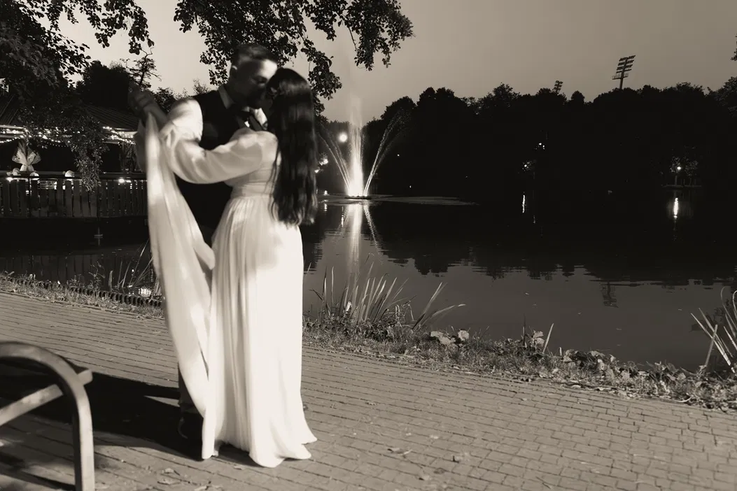 Para tańcząca w parkowej scenerii nocą, romantyczny klimatyczny wieczór nad jeziorem z fontanną, nastrojowe światła.
