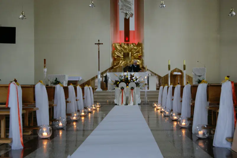  Kościół udekorowany na ślub, białe pokrowce na ławkach, świeczki w szklanych kulach, ołtarz z kwiatami. 