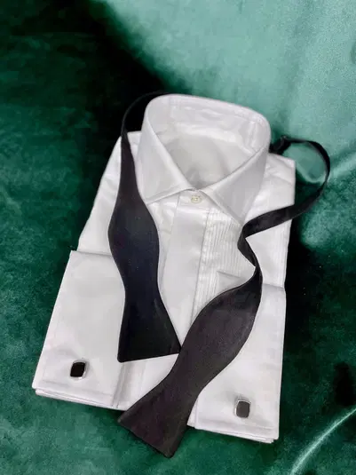  Biała koszula męska z eleganckimi spinkami i czarną muszką na zielonym tle. Idealny wybór na formalne okazje. 