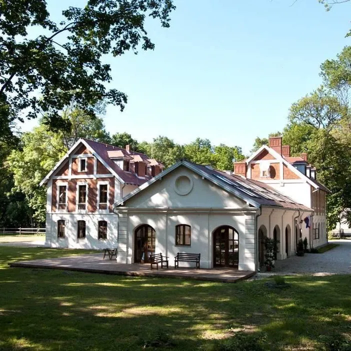 Zabytkowy budynek wśród zielonych drzew, słoneczny dzień, architektura klasycystyczna.