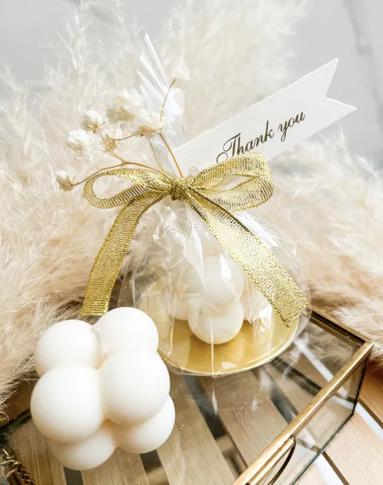 Elegancki upominek ślubny w białym opakowaniu z złotą wstążką, ozdobiony suszonymi kwiatami i kartką z napisem Thank you, idealny na podziękowanie dla gości.