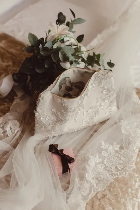Elegancka torebka ślubna z koronkowym wzorem, bukiet kwiatów eukaliptusa i różowa pudełko prezentowe na koronkowym tle.