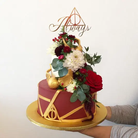  Tort inspirowany Harrym Potterem z motywem Złotego Znicza, dekorowany czerwonymi i białymi kwiatami oraz topperem z napisem Always. 