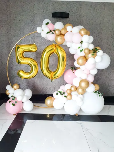  Złote balony 50, dekoracja z białych, różowych i złotych balonów, okrągła ramka na tle szarej ściany, 50. urodziny, elegancka aranżacja balonowa. 