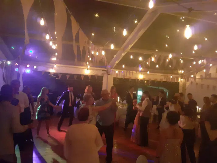 Goście bawiący się na weselnym parkiecie, dekoracje świetlne i girlandy w tle 