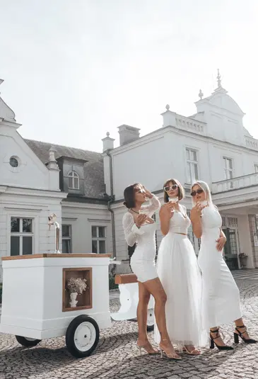  Trzy kobiety w eleganckich białych sukienkach na przyjęciu przed stylowym budynkiem. 