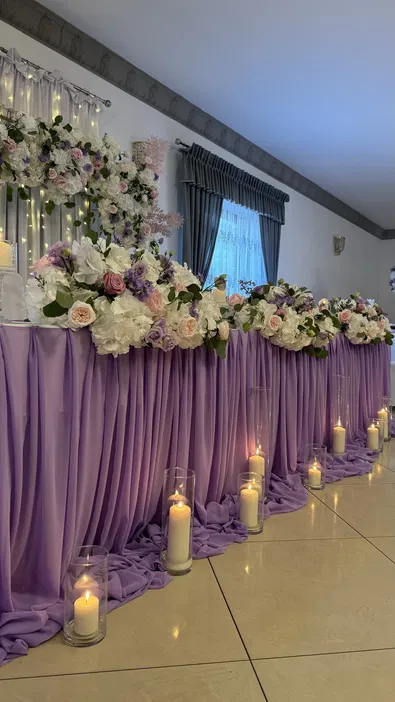 Dekoracja ślubna z fioletowym obrusem, kwiatami i świecami w eleganckiej sali weselnej.